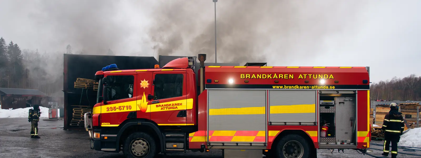 Brandbil i förgrunden framför en brinnande byggnad