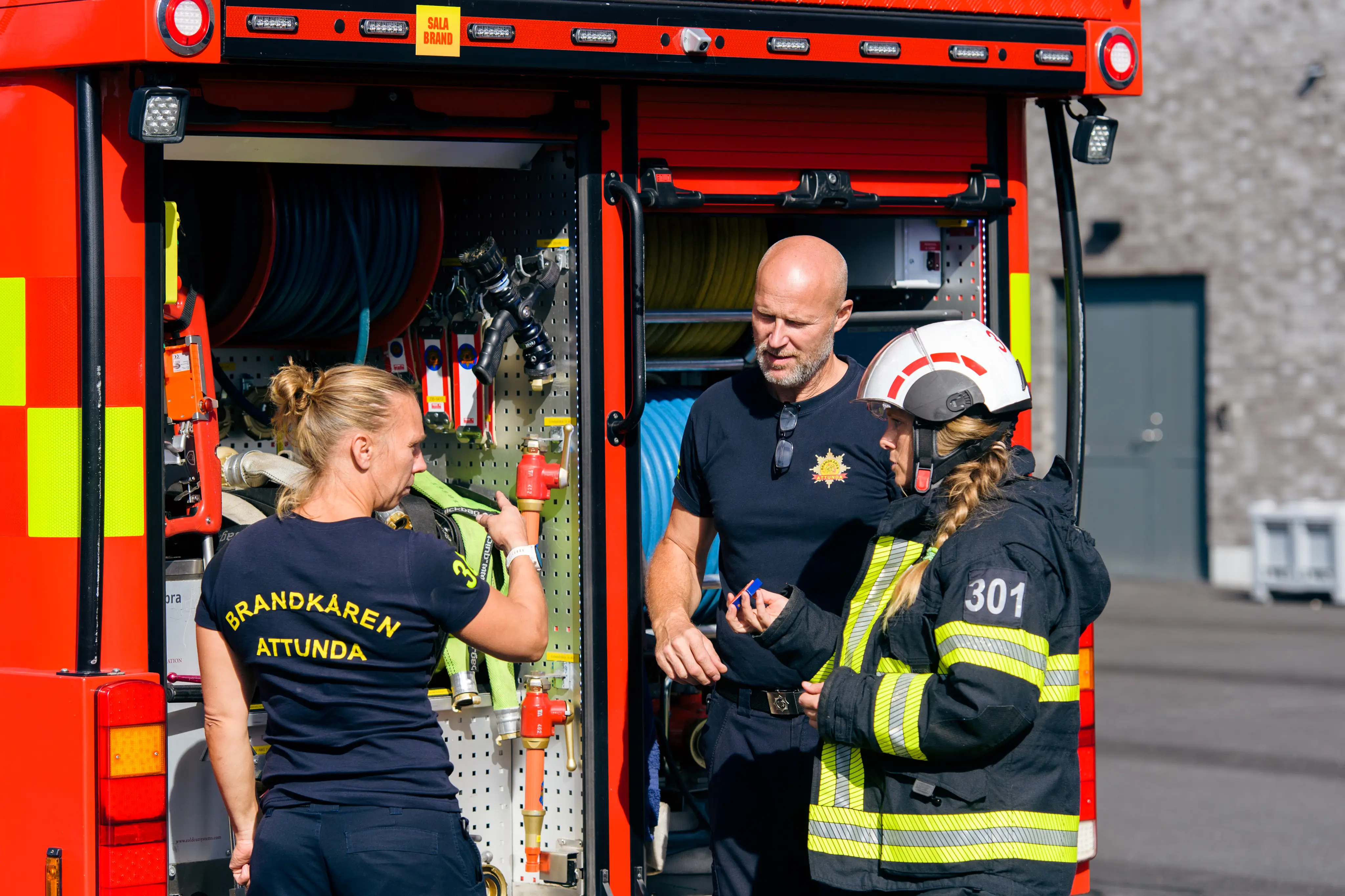 Tre brandmän pratar vid brandbil