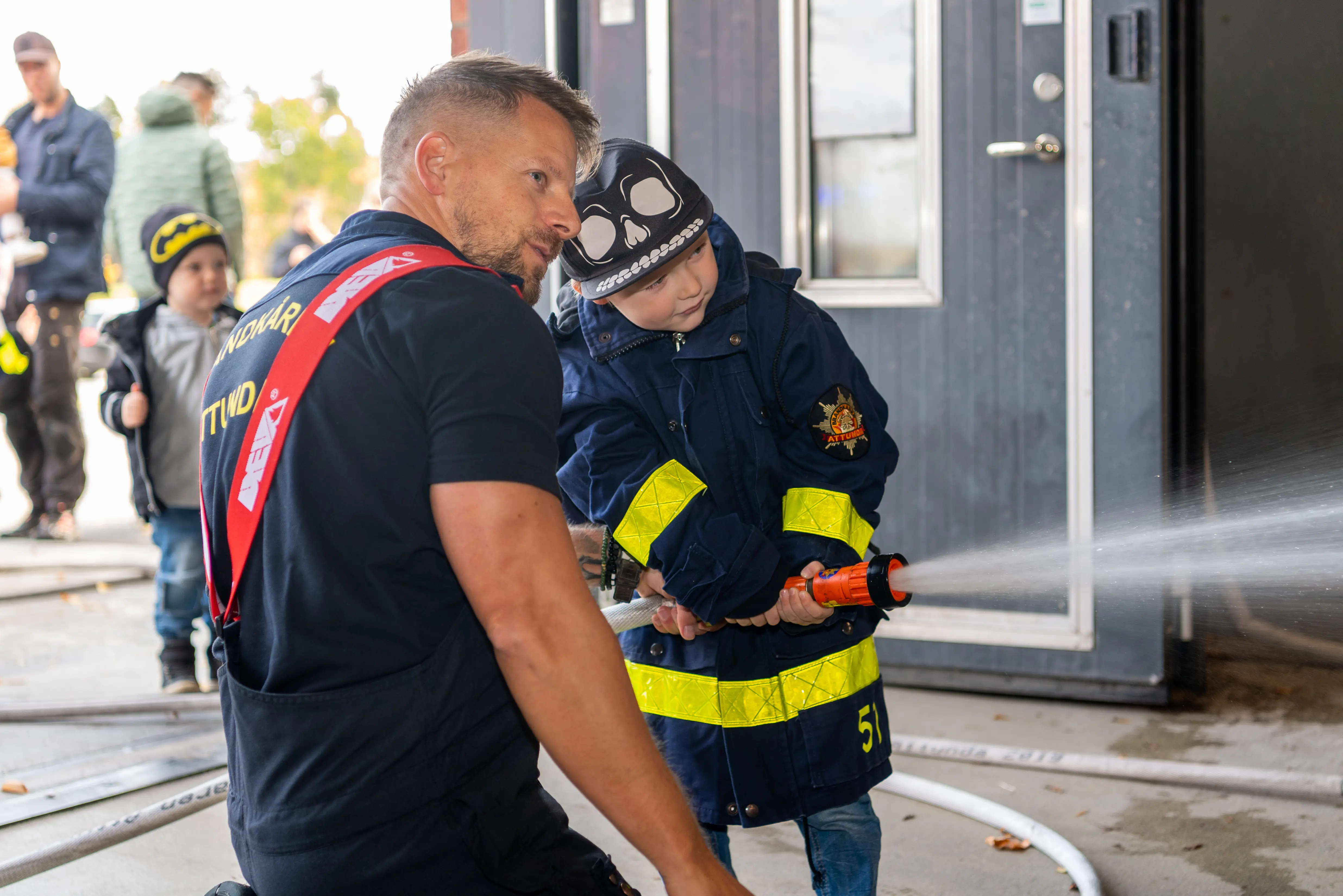Brandman hjälper barn att spruta vatten med brandslang
